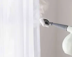 A handheld steamer is steaming white curtains