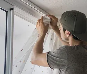 A person adjusts light gray curtains at a wall-mounted track