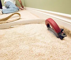 A person installing carpet near a wall