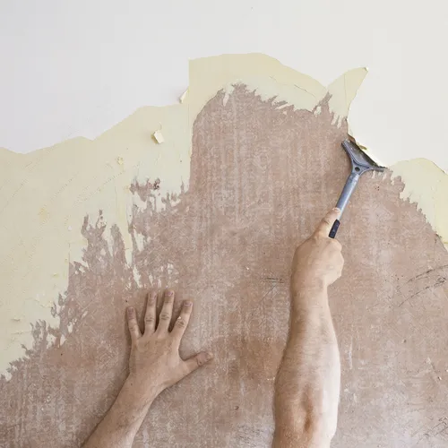 A person's hand using a scraper to remove wallpaper