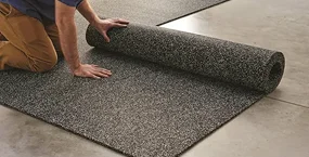 erson unrolling a gray textured carpet on a smooth concrete floor