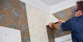 man applies wallpaper in a corner